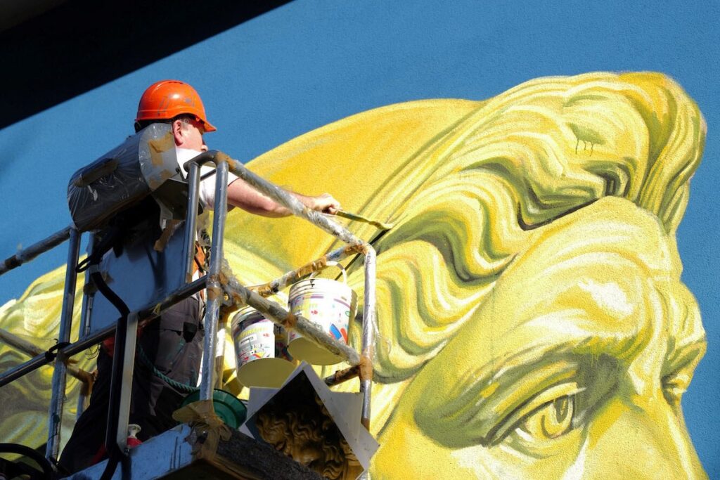 L'artista Ozmo all'opera sul murale di Giano Bifronte alla scuola "Pezzoli"