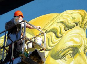L'artista Ozmo all'opera sul murale di Giano Bifronte alla scuola "Pezzoli"