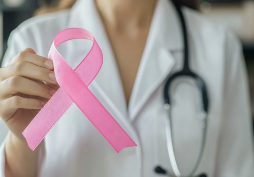 Doctor is holding a pink ribbon, representing breast cancer awareness and support for patients - prevenzione tumore al seno