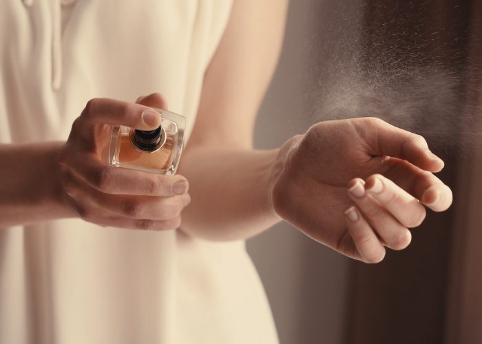 Beautiful young woman with bottle of perfume at home, closeup