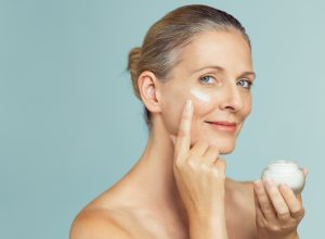 Mature woman applying skin cream on face