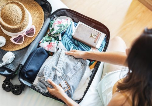 Young woman traveler sitting on the bed packing her suitcase preparing for travel on summer vacation