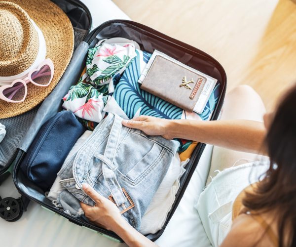 Young woman traveler sitting on the bed packing her suitcase preparing for travel on summer vacation