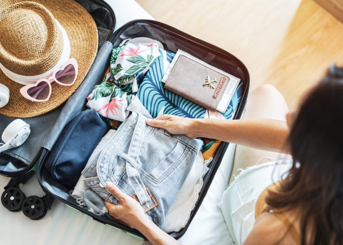 Young woman traveler sitting on the bed packing her suitcase preparing for travel on summer vacation
