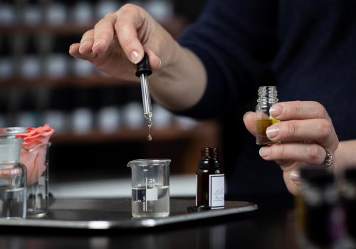 Perfumer making a perfume with tweezers Perfume bottles in the shelves in the blurry background