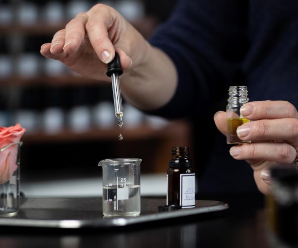 Perfumer making a perfume with tweezers Perfume bottles in the shelves in the blurry background