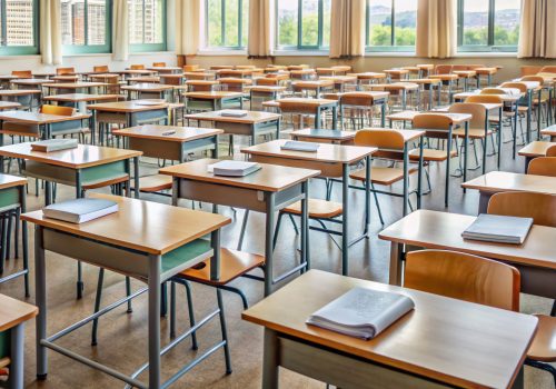 Empty classroom with rows of desks cluttered with notes, books,