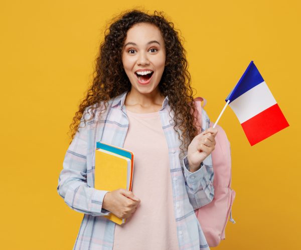 Young surprised excited cool black teen girl student she wearing casual clothes backpack bag hold books french flag isolated on plain yellow color background High school university college concept